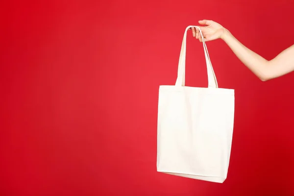 Female hand holding white cotton eco bag on red background — Stock Photo, Image