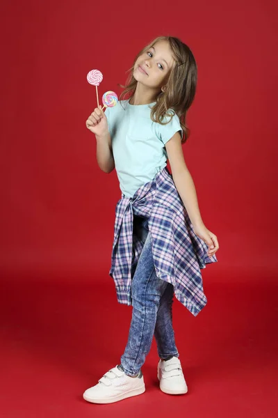 Молода дівчина в модному одязі з льодяниками на червоному тлі — стокове фото