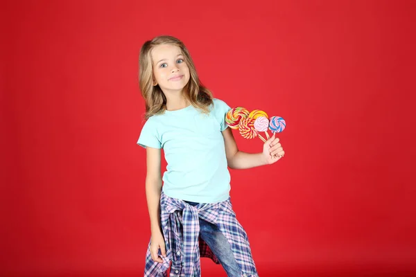 Menina com pirulitos coloridos no fundo vermelho — Fotografia de Stock