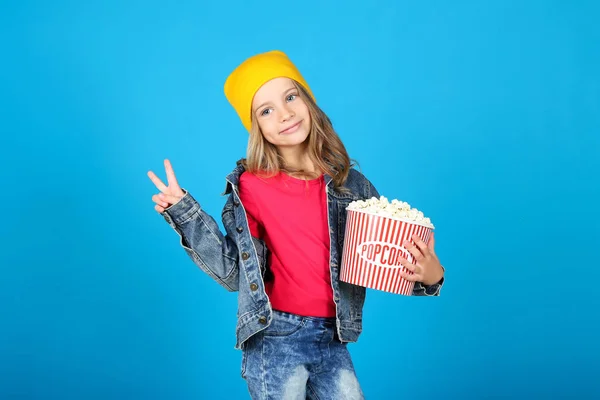 Young girl holding bucket with popcorn on blue background