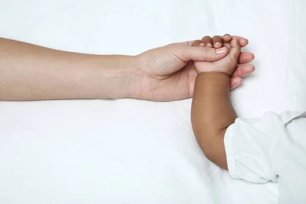 Mano de madre sosteniendo la mano de niña en cama blanca —  Fotos de Stock