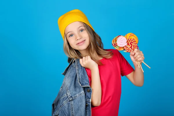 Young girl in fashion clothing with colorful lollipops on blue background