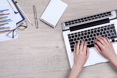 Dizüstü bilgisayarda çalışan kadın, kağıt çizelgeler ve gözlüklerle...