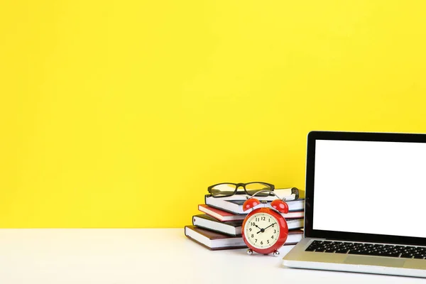 Ordinateur portable avec livres, lunettes et réveil sur ba jaune — Photo