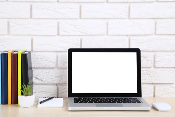 Laptop computer with books and green plant on brick wall backgro