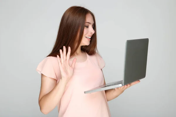 Молодая Женщина Держит Ноутбук Машет Рукой Сером Фоне — стоковое фото