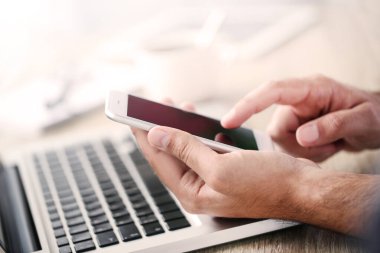 Masada dizüstü bilgisayarı olan cep telefonu kullanan bir adam