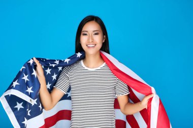 Mavi arka planda Amerikan bayrağı tutan genç bir kadın.