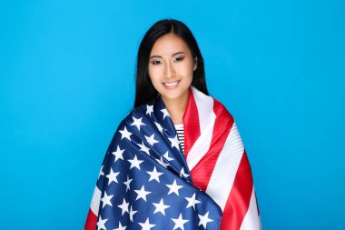 Mavi arka planda Amerikan bayrağına sarılmış genç bir kadın