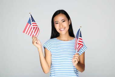Gri arka planda Amerikan bayrağı tutan genç bir kadın.