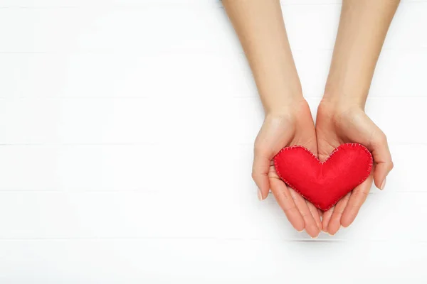 Fabric heart in female hand on white wooden table — Stock Photo, Image