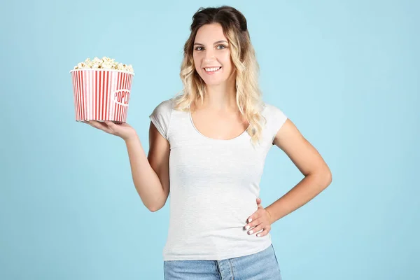 Mladá žena drží vědro s popcornem na modrém pozadí — Stock fotografie