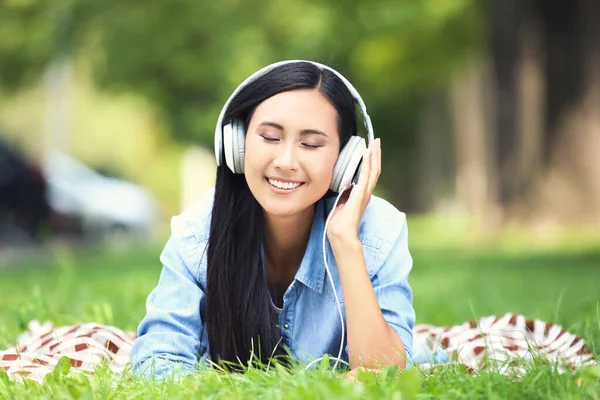 Beautiful young woman lying with headphones on green grass in th — Stock Photo, Image