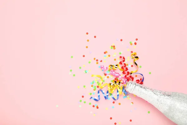 Nastri colorati con confetti e bottiglia di champagne sul retro rosa — Foto Stock