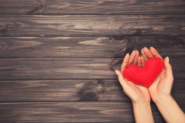 Ткань сердца в женской руке на коричневом деревянном столе — стоковое фото