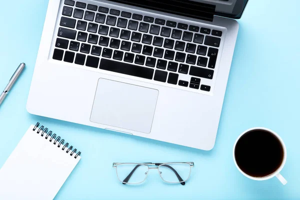 Laptop számítógép kávé, szemüveg és jegyzettömb kék háttér — Stock Fotó