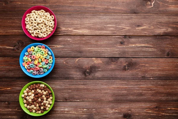 Various corn flakes in bowls on brown wooden table — Stock Photo, Image