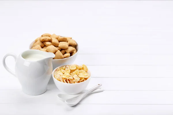 Flocos de milho com leite em jarra e colheres na mesa de madeira branca — Fotografia de Stock