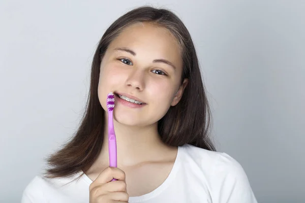 Mladá dívka s chrup rovnátka drží zubní kartáček na šedé backgro — Stock fotografie