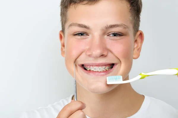 Joven con cepillo de dientes y herramienta dentista sobre fondo gris — Foto de Stock