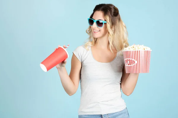 Young woman holding bucket with popcorn and paper cup on blue ba — Stock Photo, Image