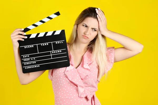 Mujer joven con tablero de aplausos en blanco sobre fondo amarillo —  Fotos de Stock