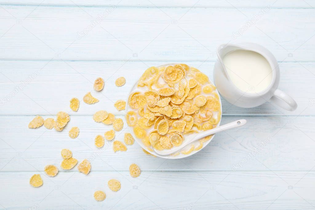 Corn flakes in bowl with milk and spoon on wooden table