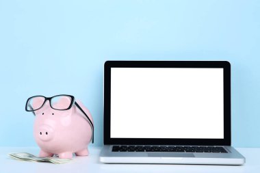 Piggybank 'lı dizüstü bilgisayar ve mavi arka planda dolar banknotları