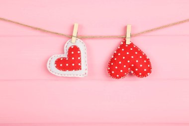 Pembe ahşap arka planda asılı mandallı kumaş kalpler.