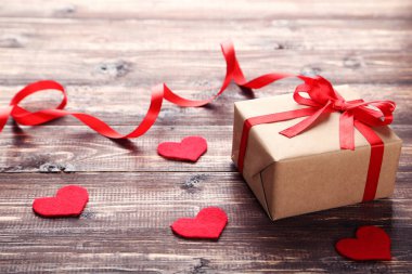 Kurdeleli hediye kutusu ve kahverengi ahşap masada kalpler.