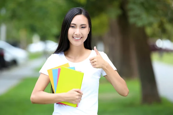 Beautiful young woman with books showing thumb up in the park — 스톡 사진