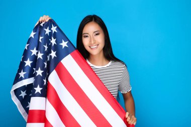 Mavi arka planda Amerikan bayrağı tutan genç bir kadın.