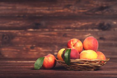 Kahverengi ahşap masa üzerinde sepet yeşil yapraklı taze şeftali