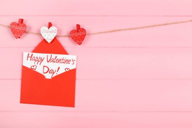 Kalpli kağıt zarf ve mesaj. Pembe ahşap arka planda asılı Sevgililer Günün kutlu olsun.
