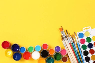 Sarı arka planda renkli guaj boyaları ve fırçalar