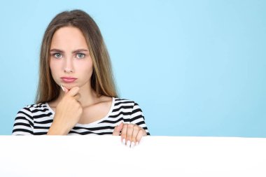 Mavi arka plan üzerinde beyaz boş tahta tutan güzel genç kadın