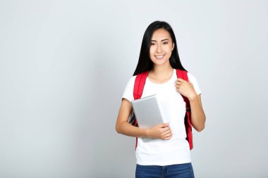 Gri poşette tablet ve sırt çantası tutan güzel genç bir kadın.