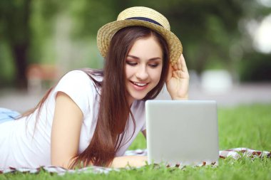 Dizüstü bilgisayarı olan şapkalı genç kız çimlerin üzerinde yatıyordu.