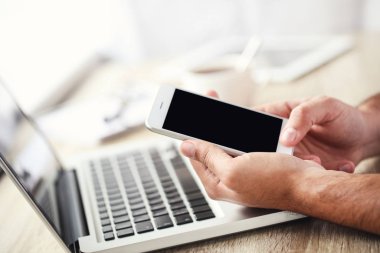 Masada dizüstü bilgisayarı olan cep telefonu kullanan bir adam