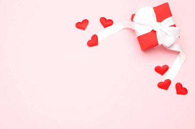 Kurdeleli hediye kutusu ve pembe arka planda kalpler.