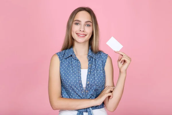Joven mujer sosteniendo tarjeta de visita en blanco sobre fondo rosa — Foto de Stock