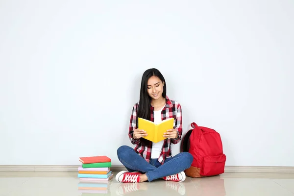 Молода жінка сидить з книгами і рюкзак на сірому фоні — стокове фото