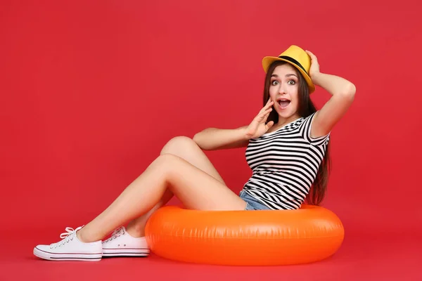 Chica joven en sombrero sentado en el anillo inflable sobre fondo rojo — Foto de Stock