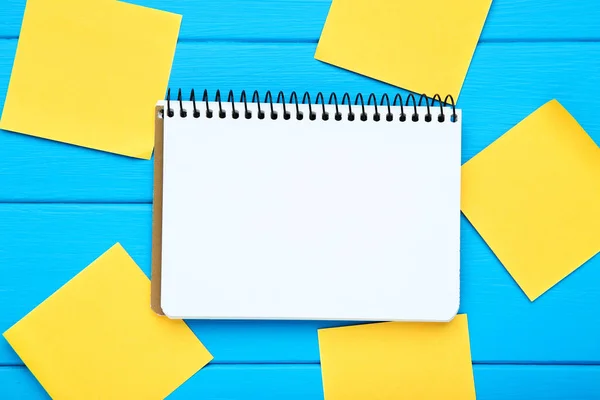 Blank notepad with paper sticky notes on blue wooden table