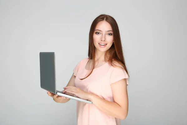Young woman using laptop computer on grey background — Stock Photo, Image