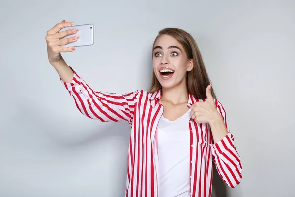 Joven hermosa chica mostrando el pulgar hacia arriba y haciendo selfie en inteligente —  Fotos de Stock