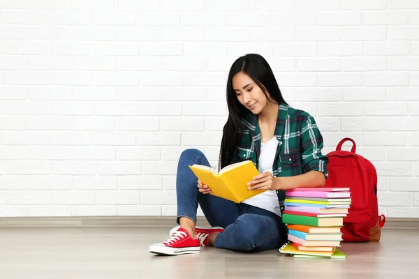 Jovem sentada com pilha de livros e mochila em branco br — Fotografia de Stock
