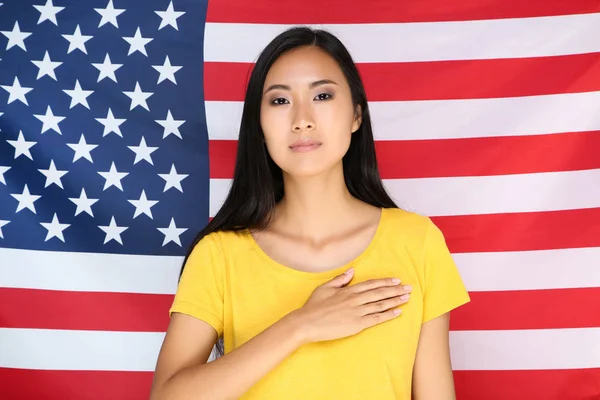 Молодая женщина с рукой на груди на фоне американского флага — стоковое фото