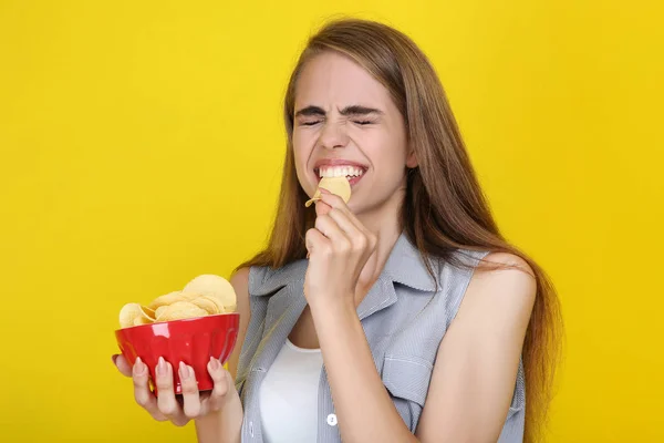 Menina bonita nova comer batatas fritas no fundo amarelo — Fotografia de Stock