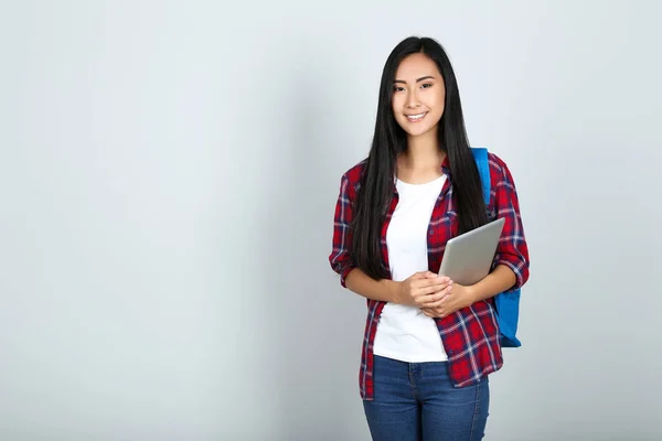 Hermosa mujer joven sosteniendo la tableta PC y la mochila en bac gris — Foto de Stock